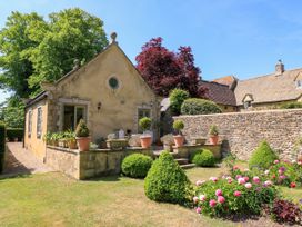A stone cottage with a garden featuring potted plants and flowering bushes at Garden Cottage in Black Bourton near Burford