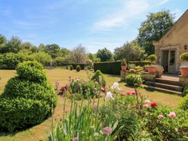 A garden with flowers bushes and potted plants next to a stone house at Garden Cottage in Black Bourton near Burford
