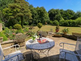 A garden patio with a white metal table and chairs a lawn with trees and plants at Garden Cottage in Black Bourton near Burford