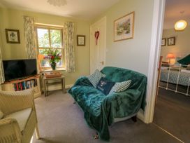 A small living room with a green-covered sofa a television a wicker chair and a window with floral curtains at Garden Cottage in Black Bourton near Burford