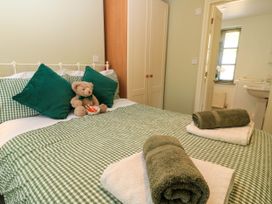 A bedroom with a bed dressed in green check bedding green and white towels on the bed a teddy bear on pillows and a wardrobe near the doorway to a bathroom at Garden Cottage in Black Bourton near Burford