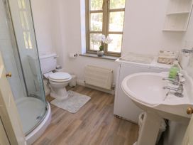 A bathroom with a shower, toilet, sink, window with flowers, and a laundry machine at Garden Cottage in Black Bourton near Burford