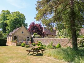 A small stone building with potted plants and a picnic table on a lawn surrounded by trees and a stone wall at Garden Cottage in Black Bourton near Burford