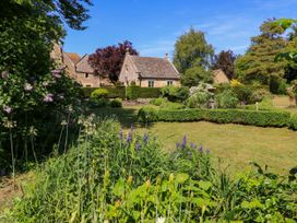 A garden with flowers shrubs and hedges in front of a stone house at Garden Cottage in Black Bourton near Burford