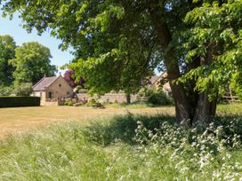 A garden with a large tree and wildflowers overlooking a stone cottage with a picnic bench and stone wall at Garden Cottage in Black Bourton near Burford