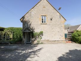 The exterior side view of a stone house with a small door under a wooden porch and one window above at Honeysuckle Cottage in Condicote
