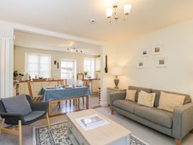 A living room with a grey sofa, armchair, and coffee table connected to a kitchen with a dining table at Honeysuckle Cottage in Condicote