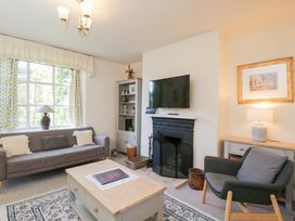 A living room with a sofa a chair a coffee table a fireplace with a TV above and shelves at Honeysuckle Cottage in Condicote