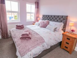 A bedroom with a bed with pillows and folded towels beside two windows and a wooden nightstand with a lamp and flowers at The Tannery in Whitby