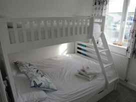 A bedroom with a white bunk bed near a window with patterned curtains at 8 Harlyn Mews in Harlyn Bay Cornwall