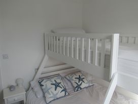A bedroom with a white bunk bed two starfish patterned pillows and a nightstand with a lamp and clock at 8 Harlyn Mews Harlyn Bay Cornwall