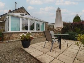 A garden with a table, chair, and umbrella near a conservatory at The Smithy in Blisland