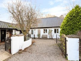 A gravel driveway leading to a white house with a bench outside and metal gates at The West Wing in Bodfari