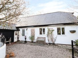 An exterior view of a white building with a slate roof two windows a door a wooden bench and gravel ground at The West Wing in Bodfari