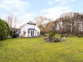 A white house with a small patio and outdoor furniture in a large grassy garden with trees at The West Wing in Bodfari