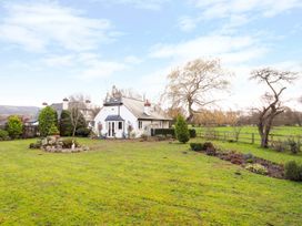 A white house with a garden and trees on a grassy lawn at The West Wing in Bodfari