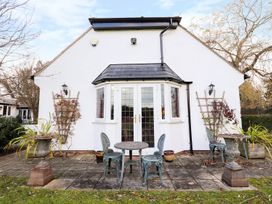 An outdoor patio area with a round table and three metal chairs in front of white double doors at The West Wing in Bodfari