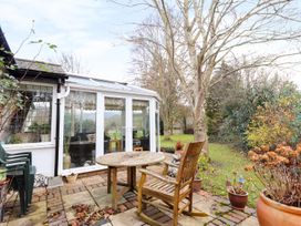 A garden patio with wooden table and chair outside a glass conservatory at The West Wing in Bodfari