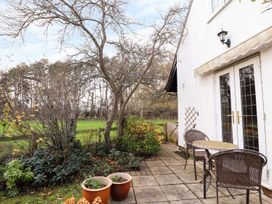 A patio with a table and two chairs next to a white house with plants and trees nearby at The West Wing in Bodfari