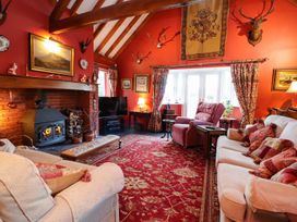 A living room with wooden beams a fireplace a red patterned carpet sofas and armchair with cushions and a television at The West Wing in Bodfari