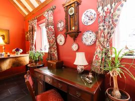 A room with a wooden desk and chair next to windows with patterned curtains and a wall clock at The West Wing in Bodfari