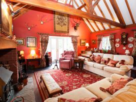 A living room with red walls wooden ceiling beams sofas armchair piano and fireplace at The West Wing in Bodfari