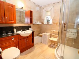 A bathroom with wooden cabinets a white sink a mirror a glass shower a toilet and a chair at The West Wing in Bodfari
