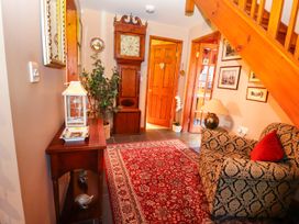 A hallway with a patterned armchair a red rug a wooden table with a lantern and decorative plate a grandfather clock and wooden stairs at The West Wing in Bodfari