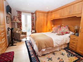 A bedroom with a double bed surrounded by wooden wardrobes a floral armchair and lamp near glass doors at The West Wing in Bodfari