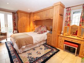A bedroom with a bed surrounded by wooden wardrobes and a vanity table with floral curtains at The West Wing in Bodfari