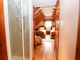 A hallway with a shower enclosure on the left and a bedroom with two single beds at The West Wing in Bodfari