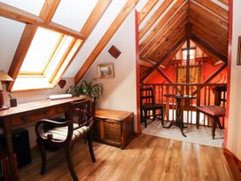 An attic room with wooden beams a desk chair and lamp and a seating area with two chairs and a table at The West Wing in Bodfari
