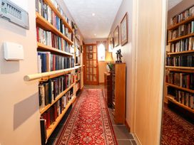 A hallway with bookshelves on the left a red patterned rug and a wooden cabinet with a lamp and sculpture at The West Wing in Bodfari