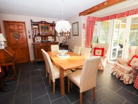 A dining room with a wooden table and six chairs a wooden cabinet two armchairs with red cushions and checked curtains at The West Wing in Bodfari