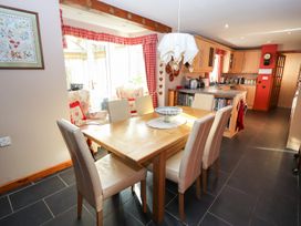 A dining area with a wooden table and six chairs next to a kitchen with wooden cabinets and a black tiled floor at The West Wing in Bodfari
