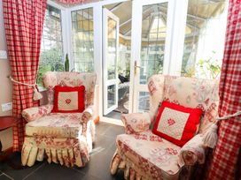 A seating area with two patterned armchairs and red cushions near glass doors leading to a sunroom at The West Wing in Bodfari