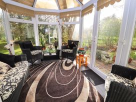 A conservatory with black wicker furniture and patterned cushions with a glass coffee table and plants at The West Wing in Bodfari
