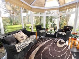 A conservatory with wicker sofa and armchairs with patterned cushions a glass table plants and a patterned rug at The West Wing in Bodfari