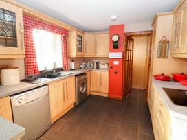 A kitchen with wooden cabinets red curtained window dishwasher washing machine and countertop appliances at The West Wing in Bodfari