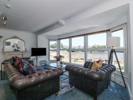 A living room with two leather sofas a glass coffee table a floor lamp and large windows overlooking a waterfront at Sea View apartment in Borth-Y-Gest