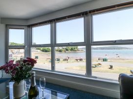 A room with a large window showing a view of a beach and people outside with a table holding flowers a bottle and glasses inside Sea View apartment Borth-Y-Gest