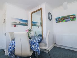 A dining area with a table covered by a blue patterned tablecloth four white chairs a large wall mirror a clock and paintings at Sea View apartment in Borth-Y-Gest