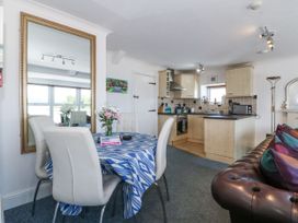 A dining area with white chairs and a blue patterned tablecloth next to a kitchen with light wood cabinets at Sea View apartment in Borth-Y-Gest