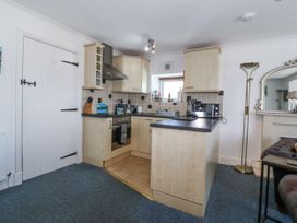 A kitchen with wooden cabinets a black countertop a stove a microwave a sink and a window at Sea View apartment in Borth-Y-Gest