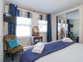 A bedroom with a bed with folded towels a chair with a blue pillow a dressing table with flowers and a wall-mounted TV at Sea View apartment in Borth-Y-Gest