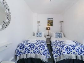 A bedroom with two single beds each with blue patterned blankets a bedside table lamp and lamps on each side at Sea View apartment in Borth-Y-Gest