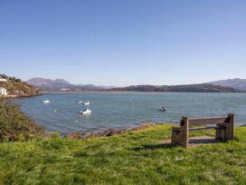 A grassy area with a bench facing a body of water with boats and hills in the background at Sea View apartment in Borth-Y-Gest