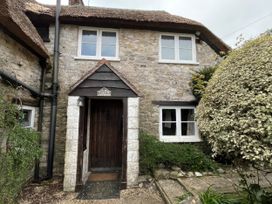 A stone cottage with a thatched roof and front door at Ivy Cottage in West Lulworth