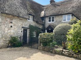 A stone cottage with a thatched roof and a garden at Ivy Cottage in West Lulworth