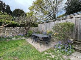 A garden with a table and chairs surrounded by trees and flowers at Ivy Cottage in West Lulworth